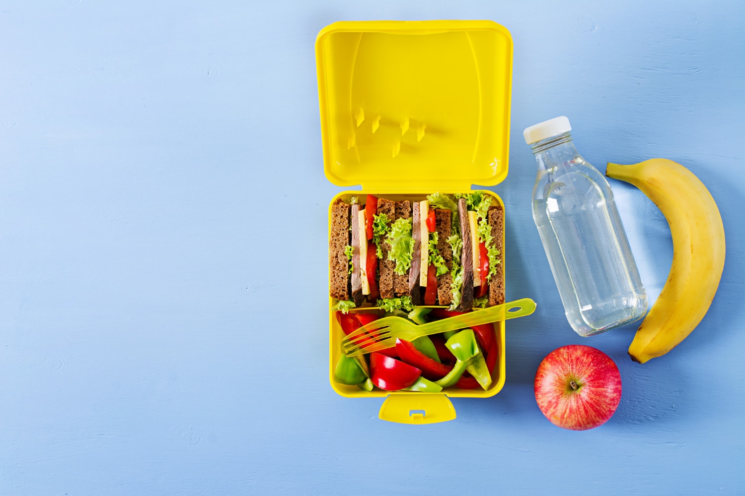healthy-school-lunch-box-with-beef-sandwich-fresh-vegetables-bottle-water-fruits-blue-table-top-view-flat-lay