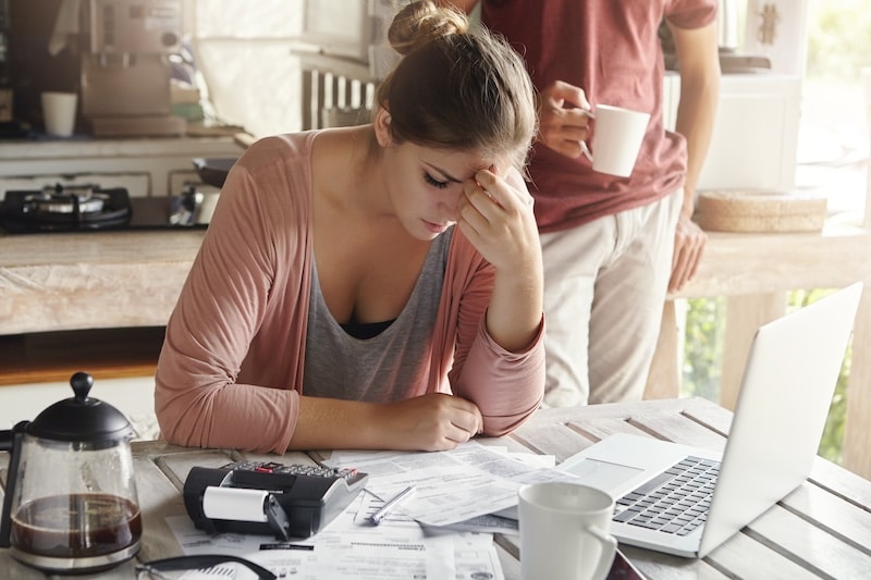 Thoughtful stressed young female sitting at kitchen table with papers and laptop computer trying to work through pile of bills, frustrated by amount of domestic expenses while doing family budget - Freepik